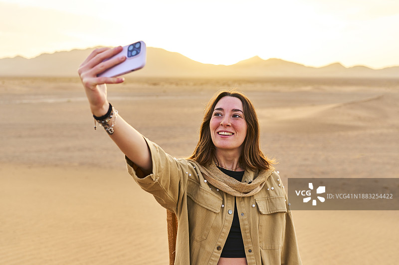 一名美丽的女游客站在萨戈拉沙漠微笑着用手机自拍，正面视图图片素材