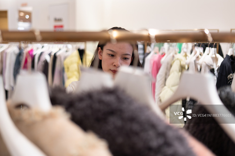 一位亚洲年轻女性在服装店挑选冬装图片素材