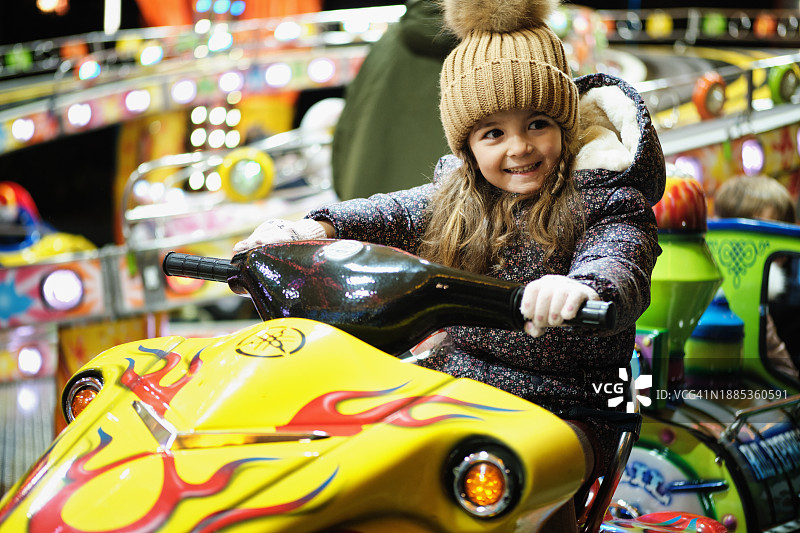 戴着流苏帽的小女孩在冬天乘坐游乐场的黄色摩托车图片素材