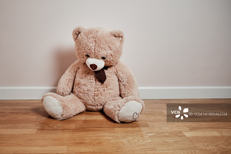 悲伤的大泰迪熊坐在木地板上，垂头丧气图片素材