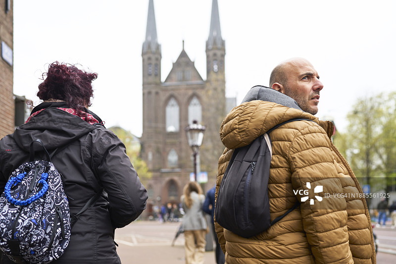 穿着外套和背包走在城市街道上的男人和女人，背景是教堂后视图图片素材