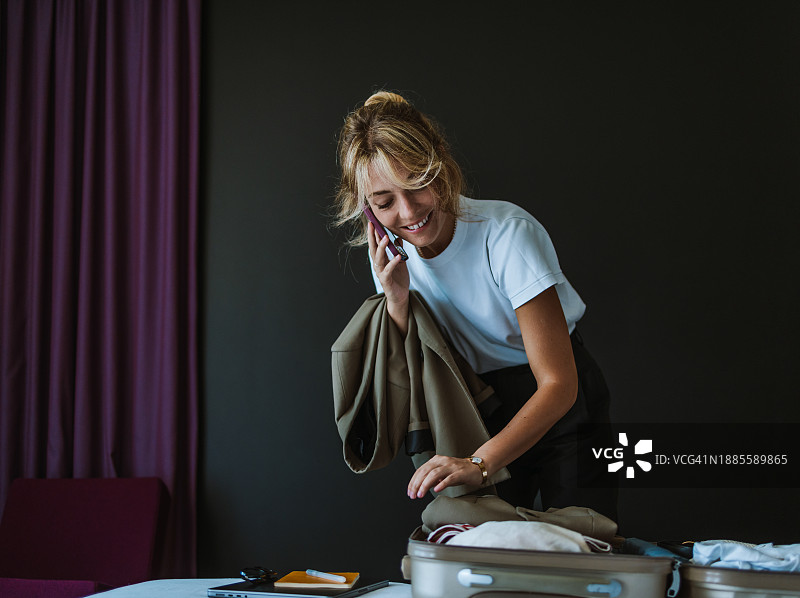 美丽的白人金发女子在打电话时整理行李箱图片素材