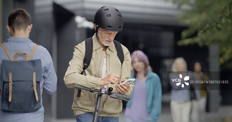 戴头盔的男人在电动滑板车旁查看手机图片素材