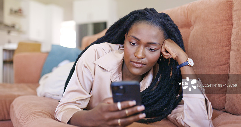 在沙发上使用智能手机放松的年轻女人图片素材