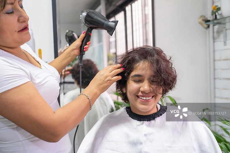快乐的年轻女人在美发沙龙里吹干头发图片素材
