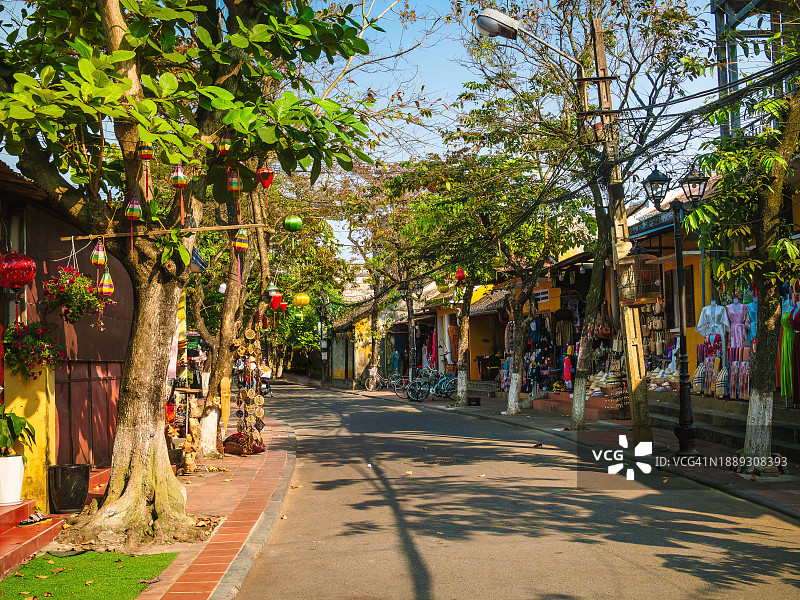 越南广南省会安古镇中，绿树成荫的步行街，两旁是色彩鲜艳的房屋、灯笼和商店的广角图图片素材