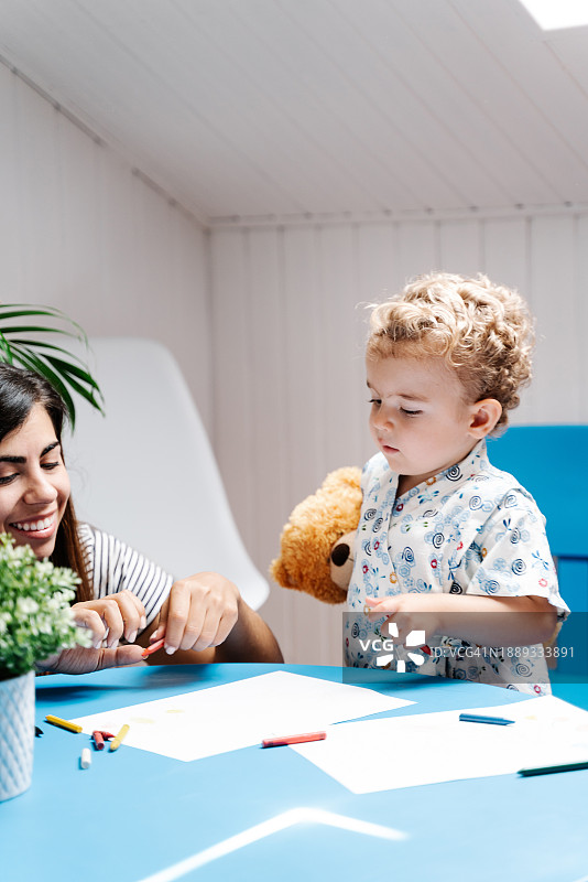 幼儿园里，微笑的母子在桌旁用铅笔画画图片素材