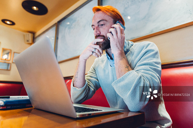 在咖啡馆使用科技产品高效处理多项任务的男士图片素材