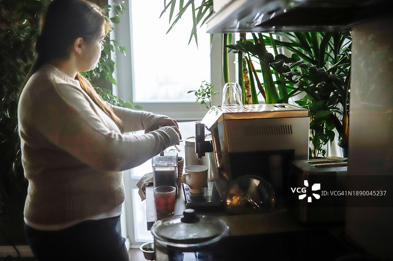 冬季早晨，疲惫的加大码女人在家用咖啡机制作咖啡，气氛压抑图片素材