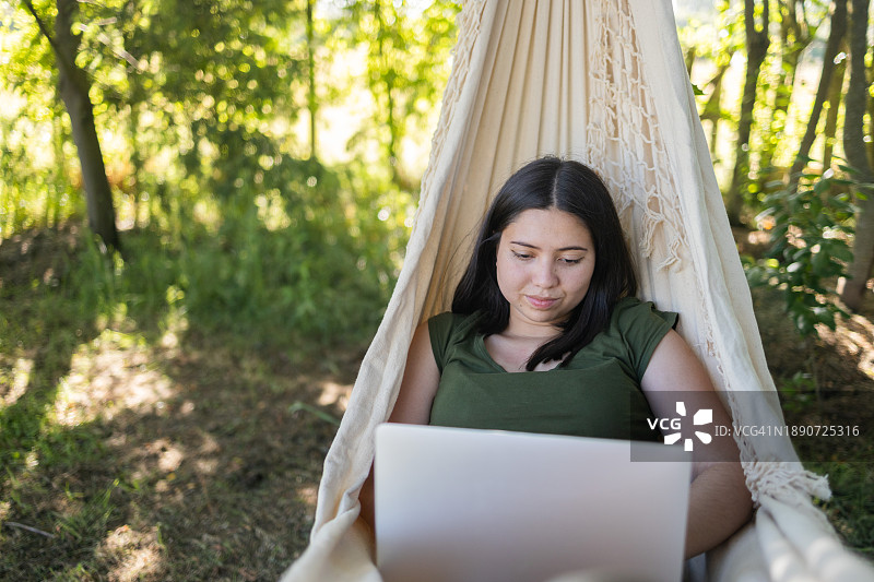 高效办公：年轻拉丁裔女子在吊床上用笔记本电脑进行远程工作图片素材