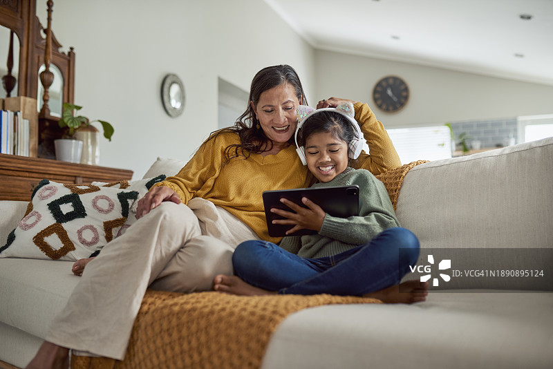 可爱的小女孩戴着耳机和微笑的祖母坐在沙发上图片素材