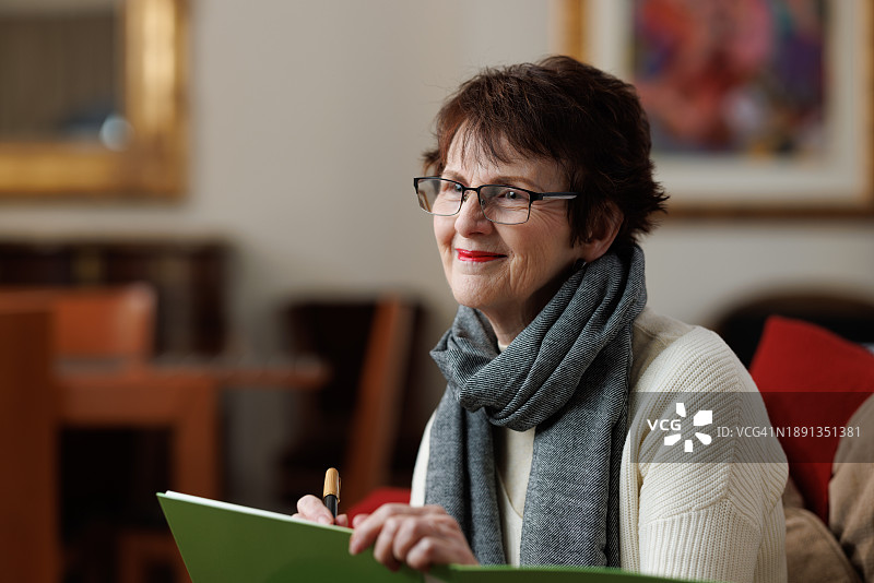 快乐的年长女性在家中使用笔和文件夹图片素材