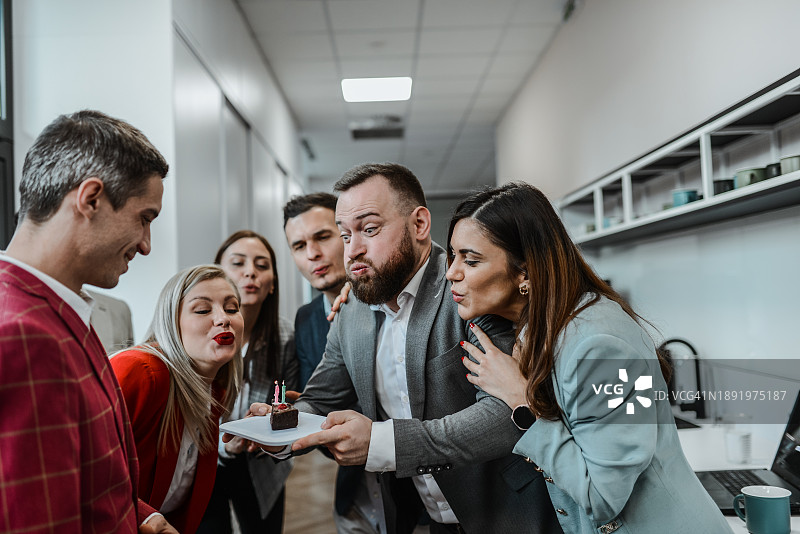 同事们帮助男CEO吹生日蛋糕蜡烛图片素材