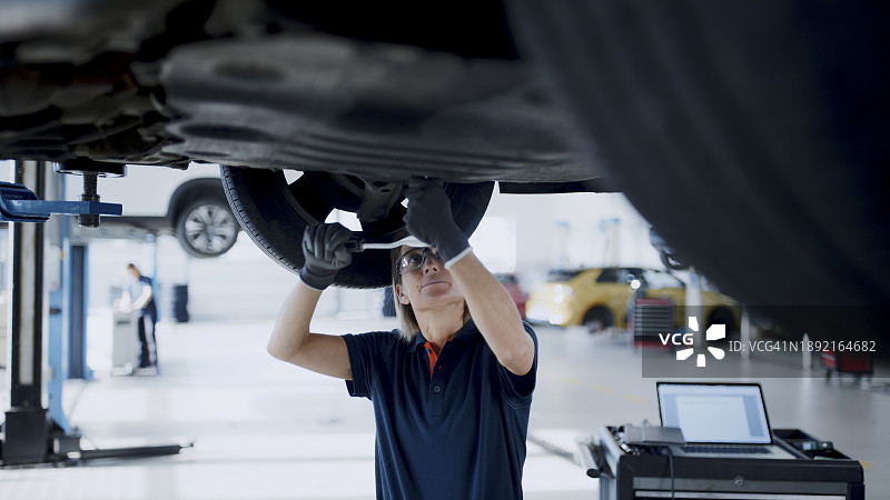 在汽车修理店车底工作的女机械师图片素材