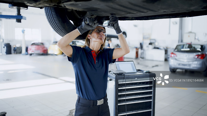 在汽车修理店车底工作的女机械师图片素材