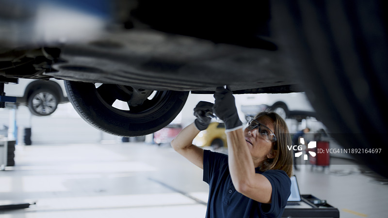 在汽车修理店车底工作的女机械师图片素材