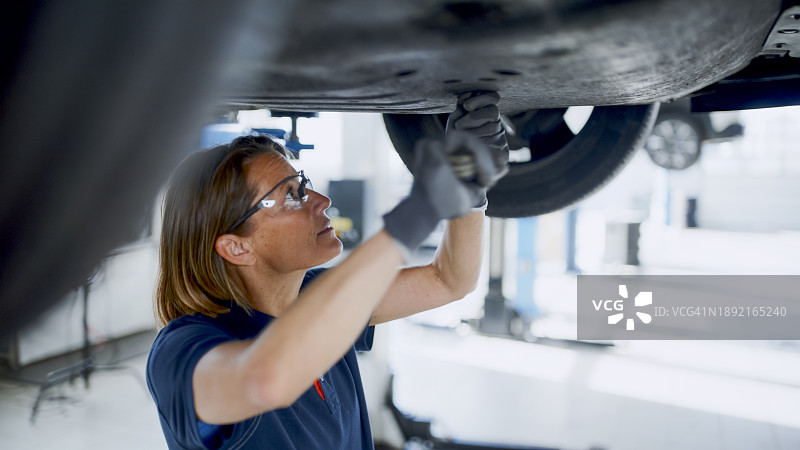 在汽车修理店车底工作的女机械师图片素材