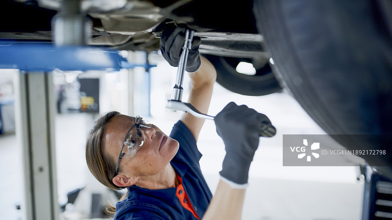 在汽车修理店车底工作的女机械师图片素材