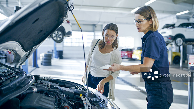 女机械师在修理店向顾客展示油尺图片素材