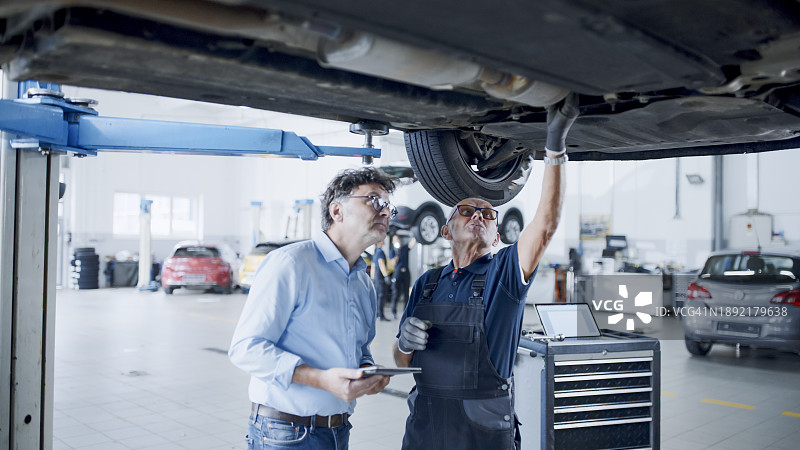 汽车修理店里，机械师和经理在车下交谈图片素材