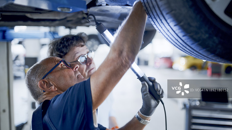 车间内，男修理工和经理在车底讨论维修事宜图片素材