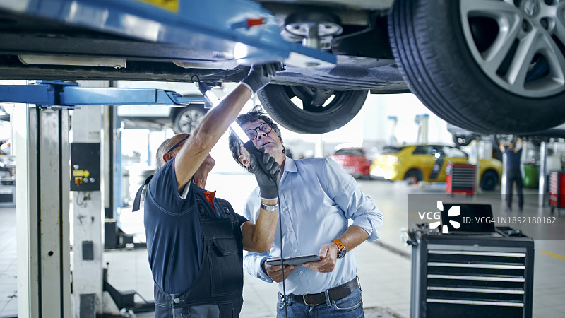 车间内，男修理工和经理在车底讨论维修事宜图片素材