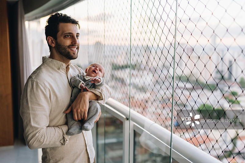 父亲在公寓阳台抱著新生女儿沉思图片素材
