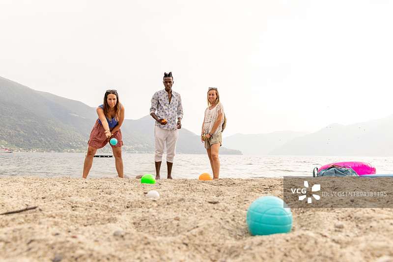 三名成年人在湖边沙滩上玩滚球图片素材