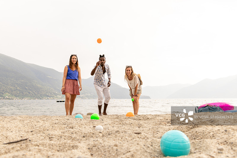 三名成年人在湖边沙滩上玩滚球图片素材