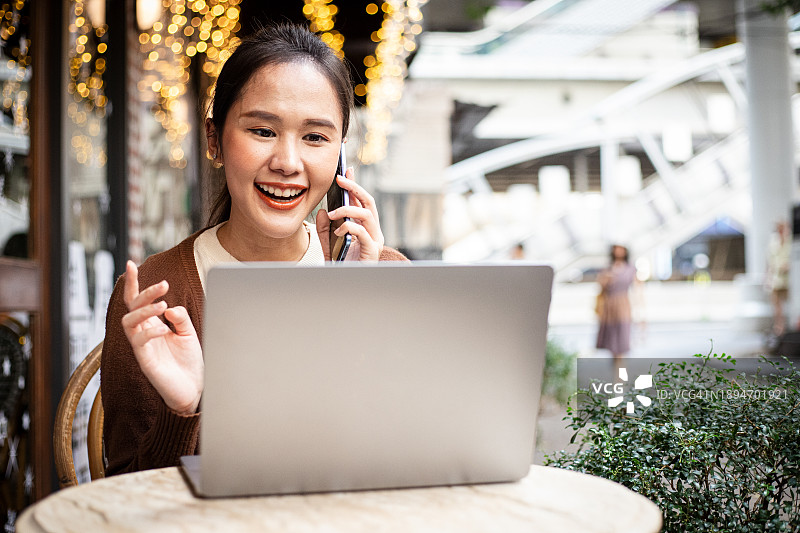 坐在室外咖啡馆用笔记本电脑工作的年轻亚洲女性图片素材