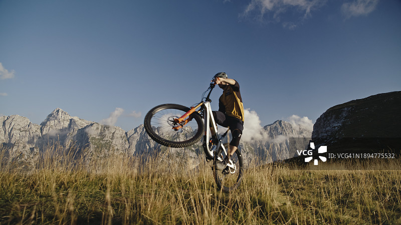 蓝天下，男子在草地上表演自行车特技的低角度景观图片素材