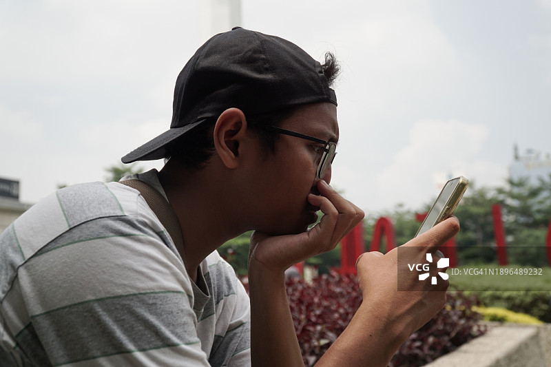 在公园使用手机的亚洲男孩图片素材
