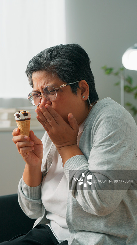 年长的亚裔祖母因敏感牙齿在吃冰淇淋时感到不适，患有牙科疾病的老年妇女，因冷热食物引起的牙痛图片素材