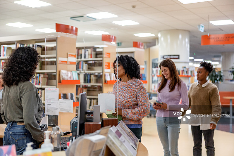 友善的拉丁美洲学生在当地大学图书馆借书图片素材
