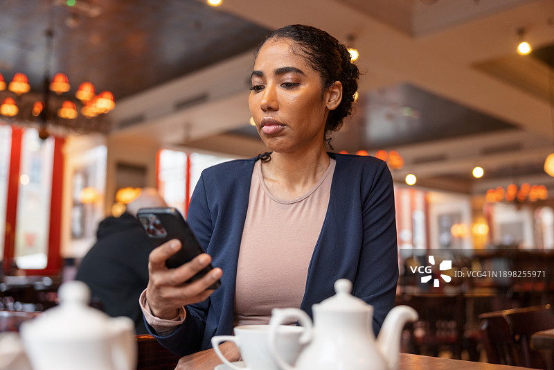在咖啡馆使用手机的深色皮肤女性肖像图片素材