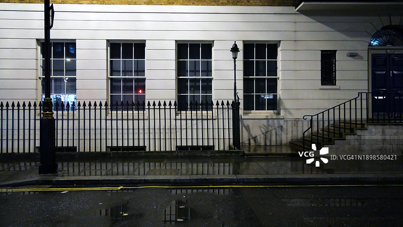 夜晚建筑白色外墙特写,有栏杆、窗户、楼梯和门。街道和人行道被雨水打湿。伦敦,英国,联合王国。没有人。图片素材