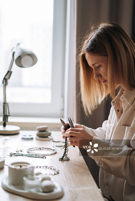 年轻珠宝设计师在工作室的工作台上制作项链图片素材