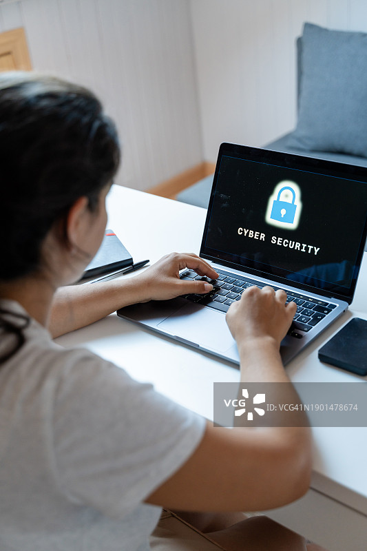 女子在家中客厅使用笔记本电脑，屏幕上显示在线安全概念图片素材