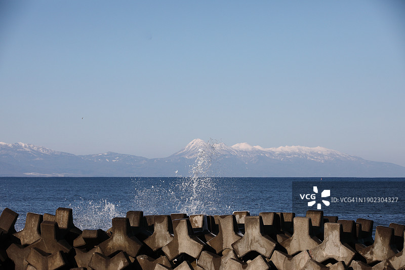 海浪拍打海滩上的混凝土防波堤，背景是雪山图片素材