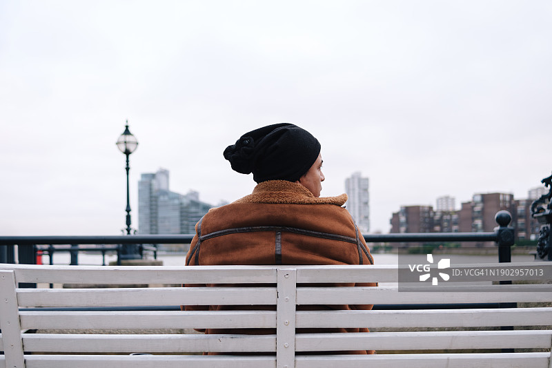 戴毛线帽的男人独自坐在海滨长椅上图片素材