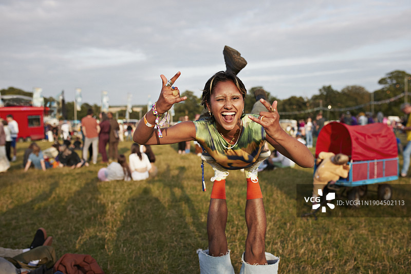 快乐的女人腿上平衡时展示摇滚手势图片素材