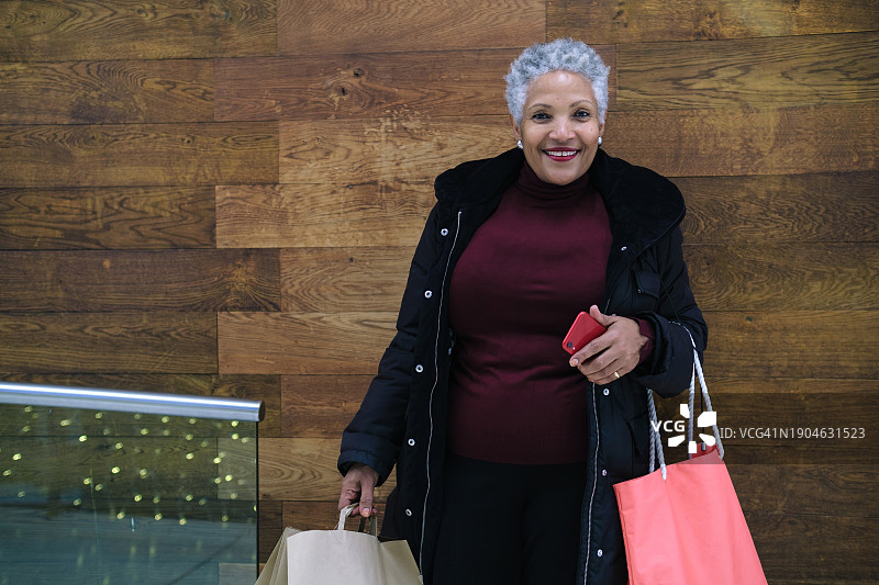 手提购物袋和红色智能手机的年长女性图片素材