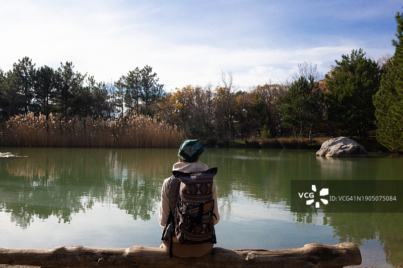 女子坐在湖边岩石上，以天空为背景图片素材
