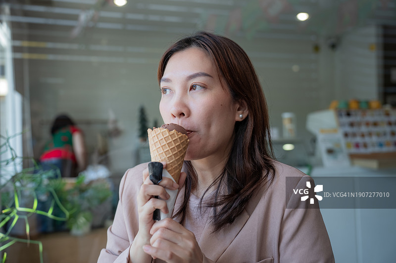 在咖啡馆吃冰淇淋，同时对牙痛病症表现出担忧表情的亚洲女性图片素材
