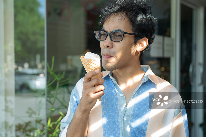 亚洲男人吃冰淇淋，牙齿敏感面露担忧图片素材