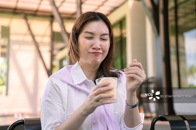快乐的女人坐在咖啡馆里，用勺子吃冷饮，以缓解敏感牙齿引起的疼痛图片素材