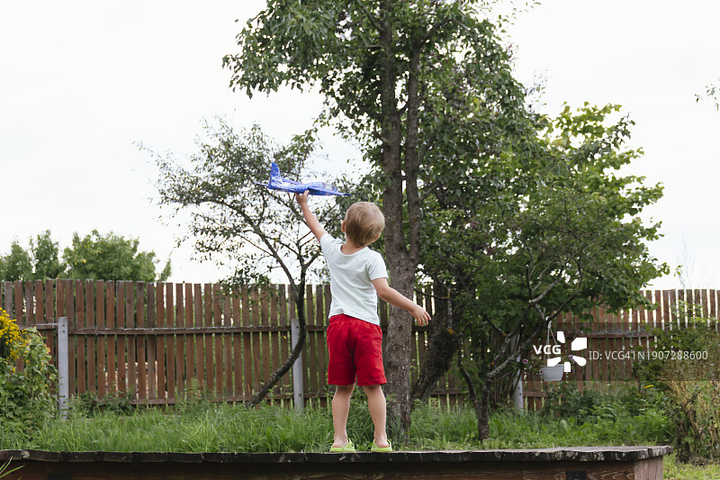 快乐的男孩在阳光明媚的夏日里放飞蓝色儿童飞机图片素材