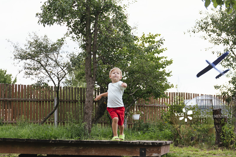 快乐的男孩在阳光明媚的夏日里放飞蓝色儿童飞机图片素材