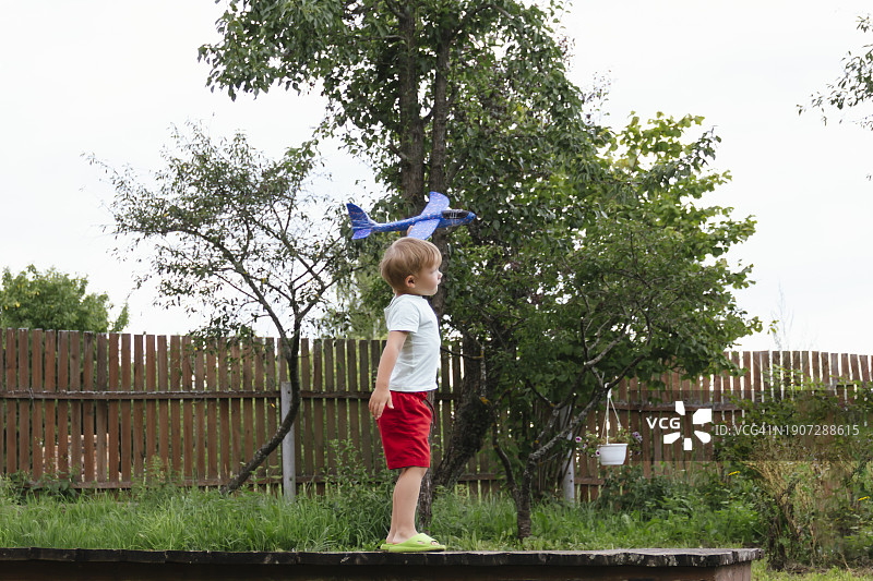 快乐的男孩在阳光明媚的夏日里放飞蓝色儿童飞机图片素材