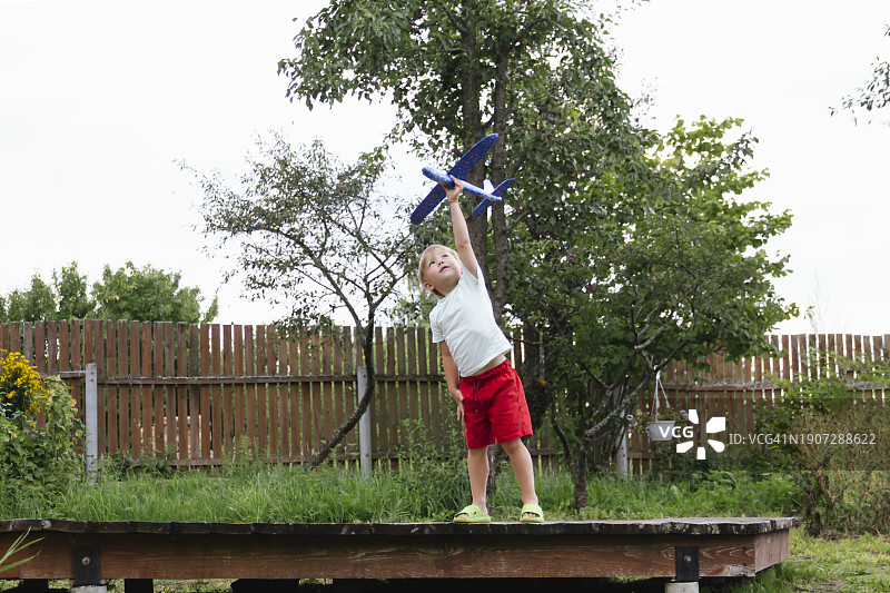 快乐的男孩在阳光明媚的夏日里放飞蓝色儿童飞机图片素材